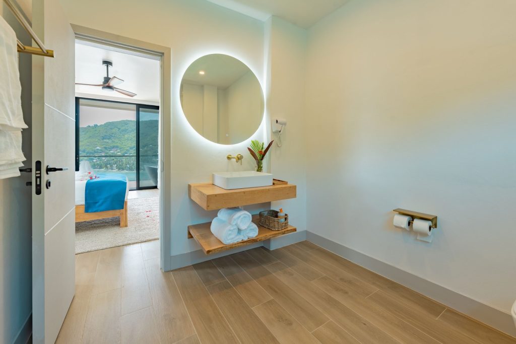 Penthouse bathroom vanity with a round lit mirror, the bedroom beyond