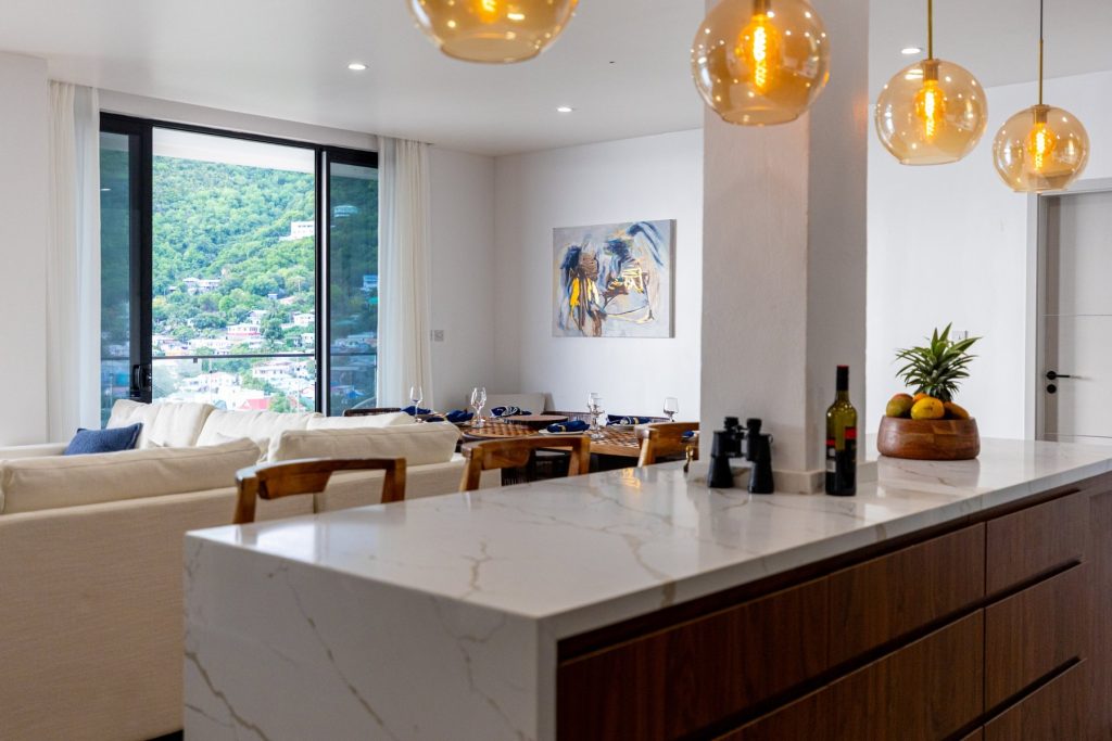 Pool Villa kitchen island with amber pendant lights, with the living and dining area beyond